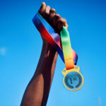 Hand holding a first-place medal against blue sky.