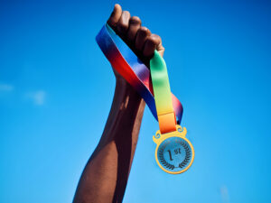 Hand holding a first-place medal against blue sky.